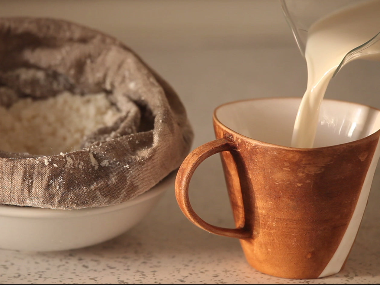 Almond Milk Is Poured Into A Cup. In The Background Lies A Line Nut Milk Bag With Almond Pulp.