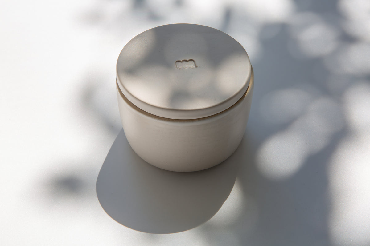 A ceramic French butter keeper with a matte white finish, sitting on a flat surface with a shadow cast over it.