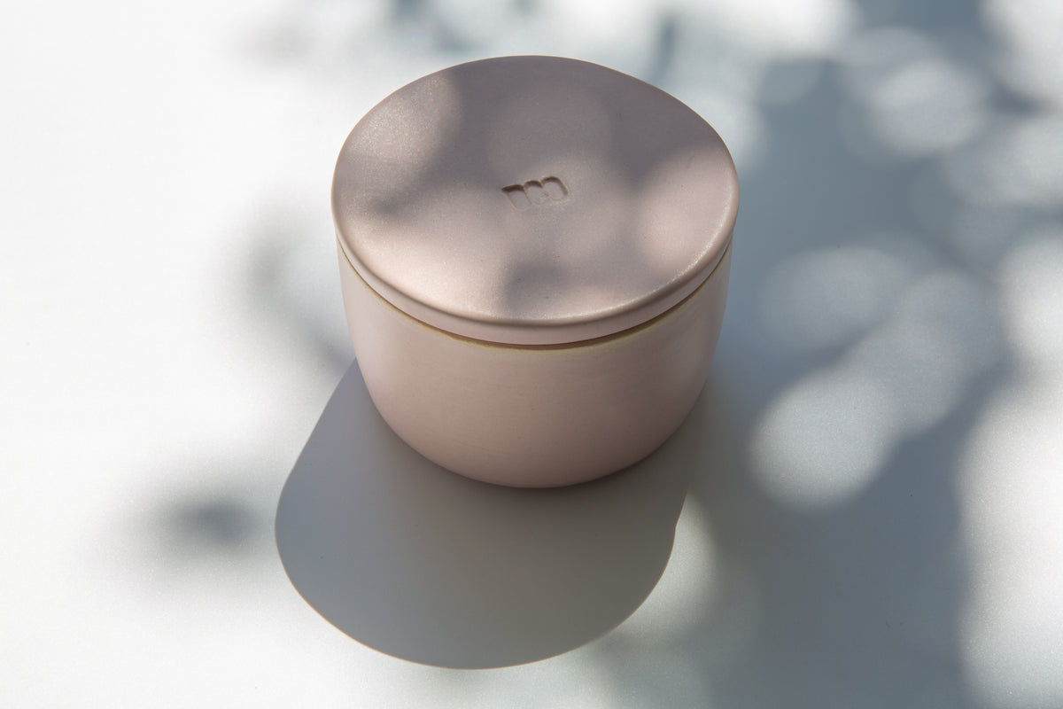 A ceramic French butter keeper with a matte pink finish, sitting on a flat surface with a shadow cast over it.