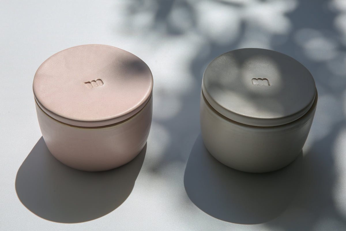 Two ceramic French butter keepers with a matte pink and white finish, sitting on a flat surface with a shadow cast over it.